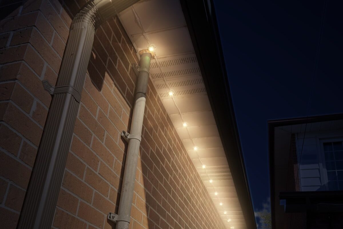 Permanent lights along the side of a brick house, shown in warm white at night